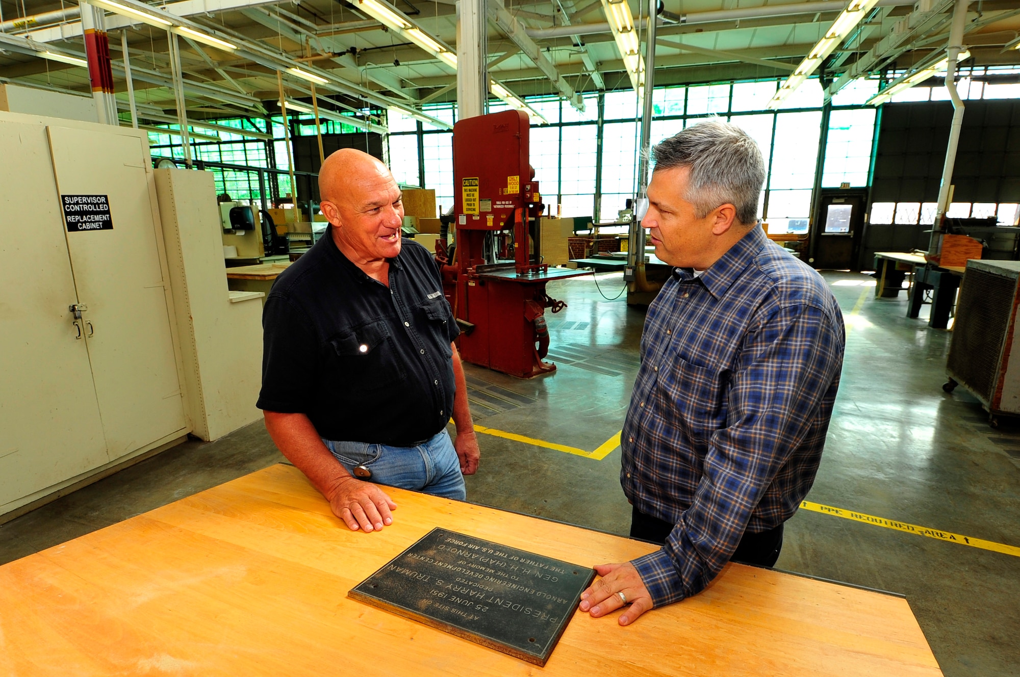 AEDC Historian Christopher Rumley, right, and Ron Bandy, left, supervisor in AEDC Carpenter and Paint Shop, talk about the history of the original AEDC Dedication Plaque. (U.S. Air Force photo/Rick Goodfriend) 