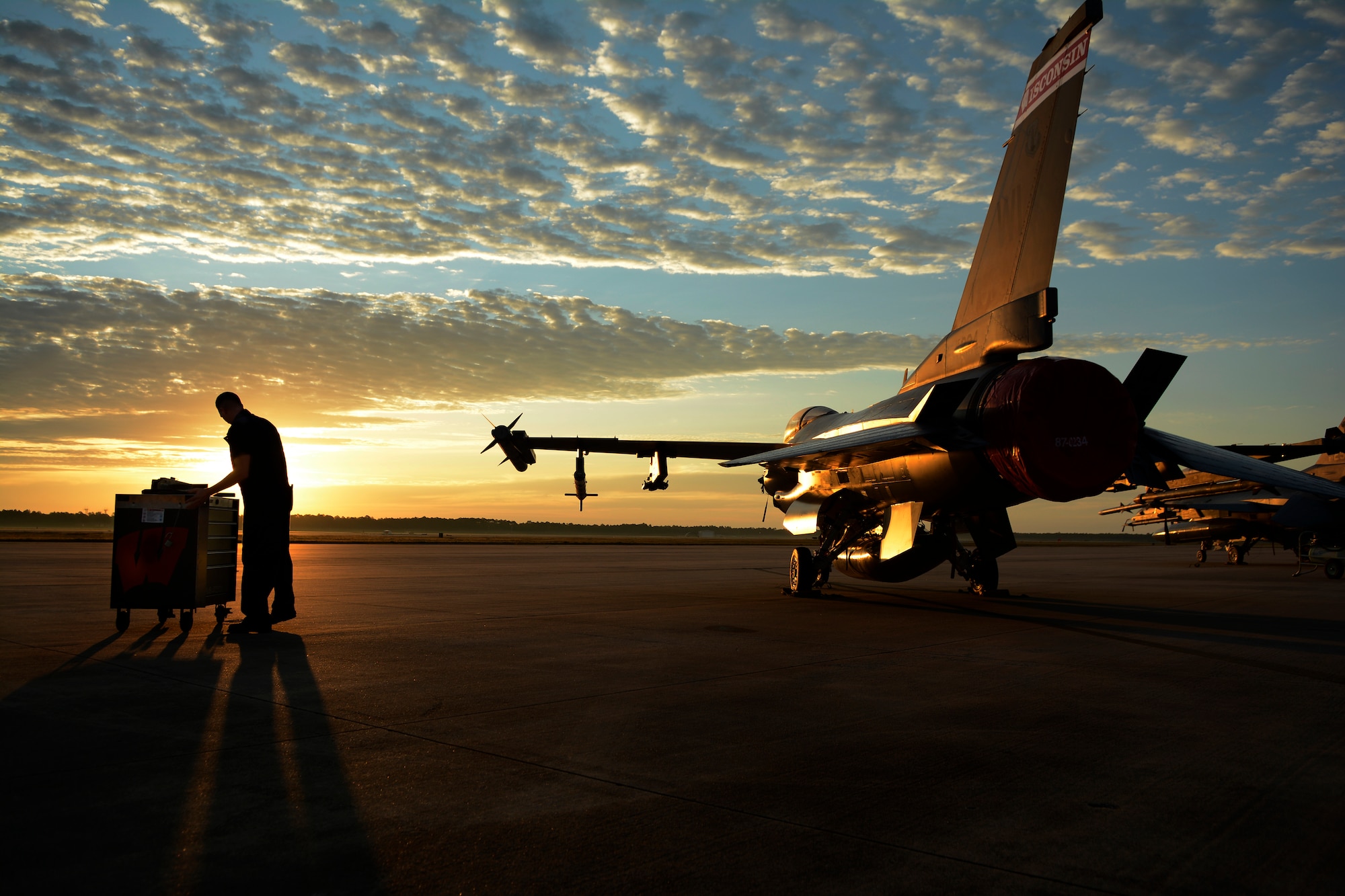 A U.S. Air Force Airman works on an F-16 Fighting Falcon during sunset.