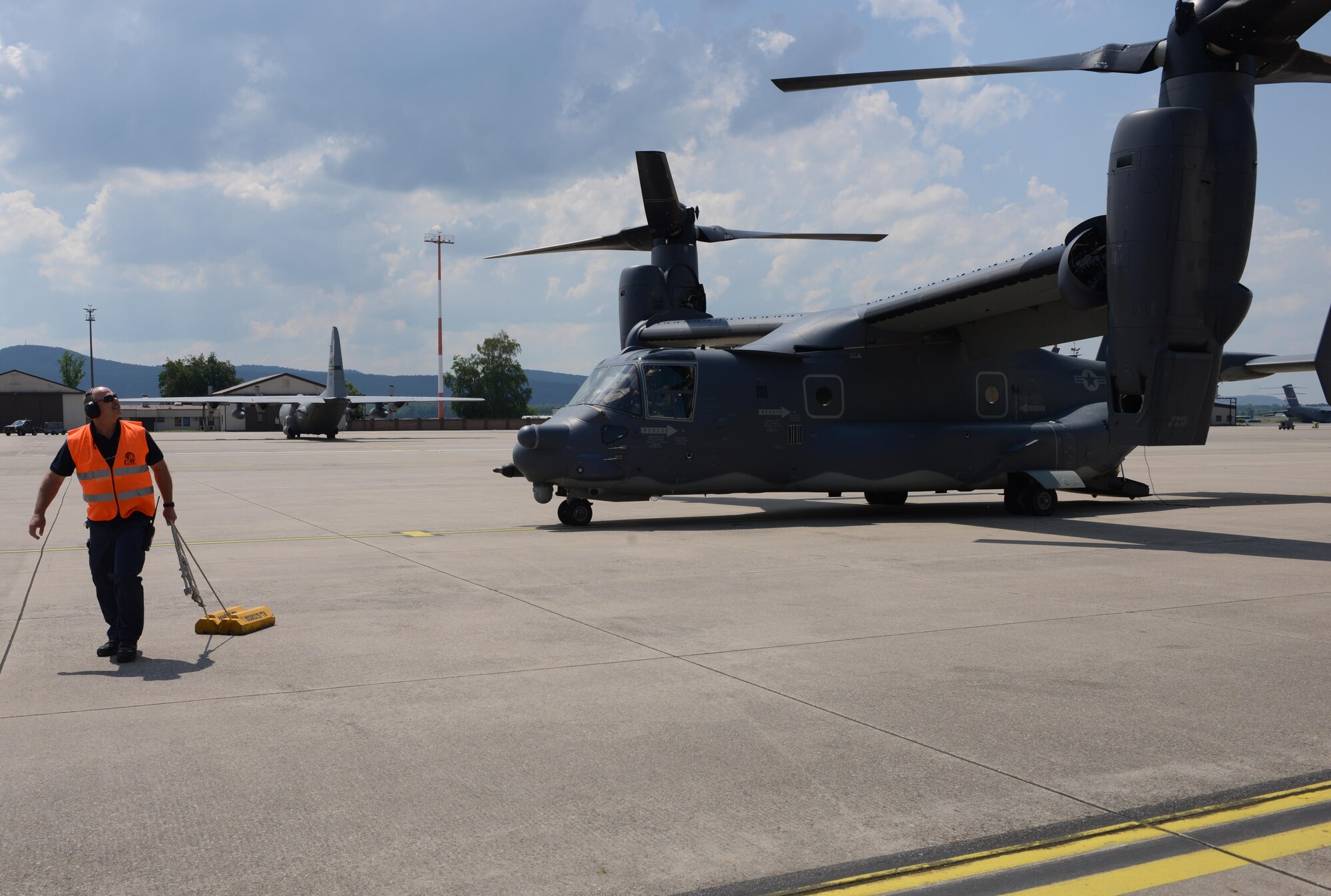 A flightline worker at Ramstein Air Base, Germany, pulls chocks as a CV-22 Osprey from the 7th Special Operations Squadron at Royal Air Force Mildenhall, England, taxis for take-off June 6, 2016. The CV-22 crew transitted through Ramstein after participating in the D-Day Remembrance airdrops in Normandy, France. (U.S. Air Force Photo/ Airman 1st Class Joshua Magbanua)

