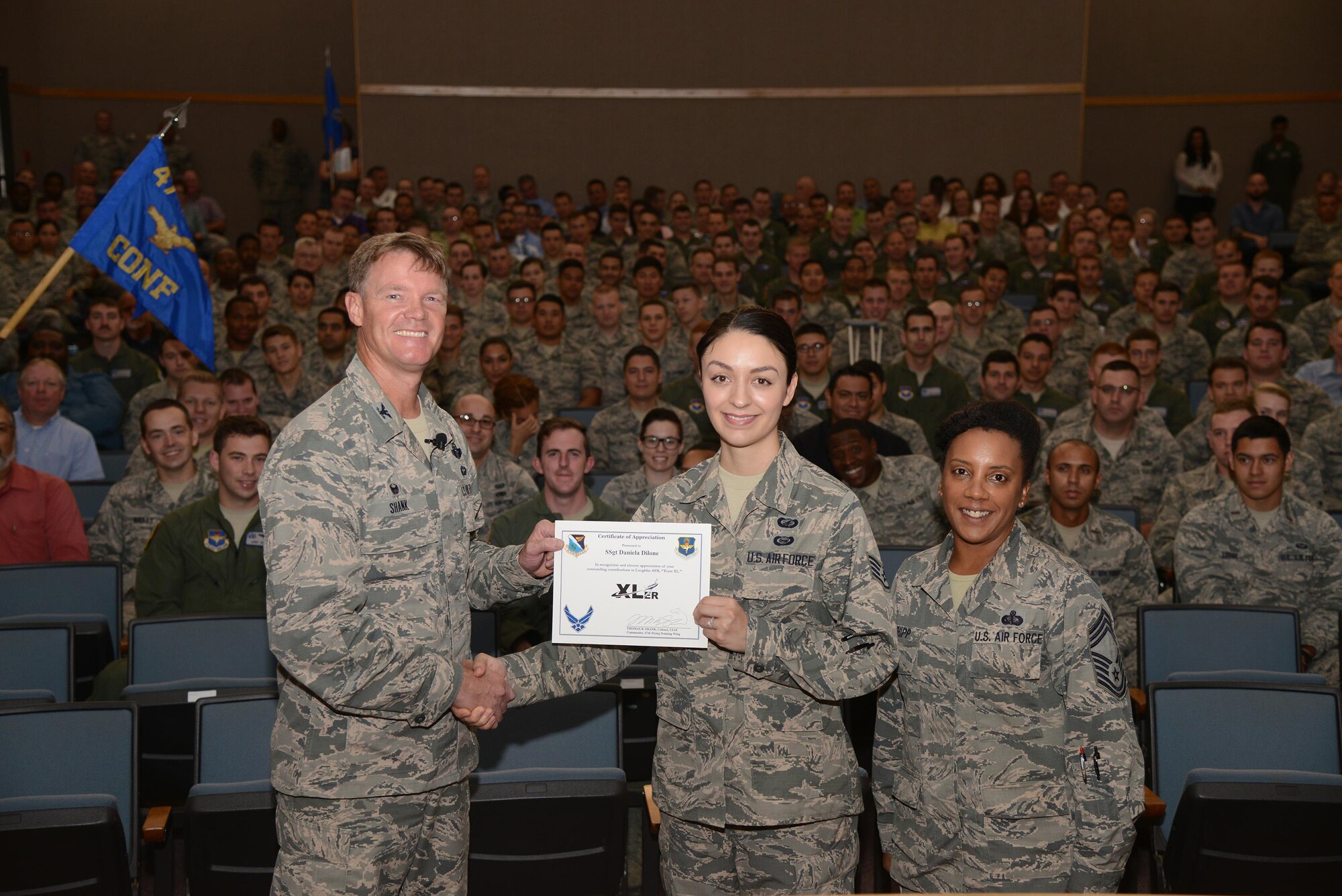 Staff Sgt. Daniela Dilone, 47th Contracting Flight contract specialist, accepts the “XLer of the Week” award from Col. Thomas Shank, left, 47th Flying Training Wing commander, and Chief Master Sgt. Erica Shipp, 47th Mission Support Group superintendent, here, during an all-call, June 2, 2016. The XLer is a weekly award chosen by wing leadership and is presented to those who consistently make outstanding contributions to their unit and Laughlin. (U.S. Air Force photo/Airman 1st Class Brandon May)