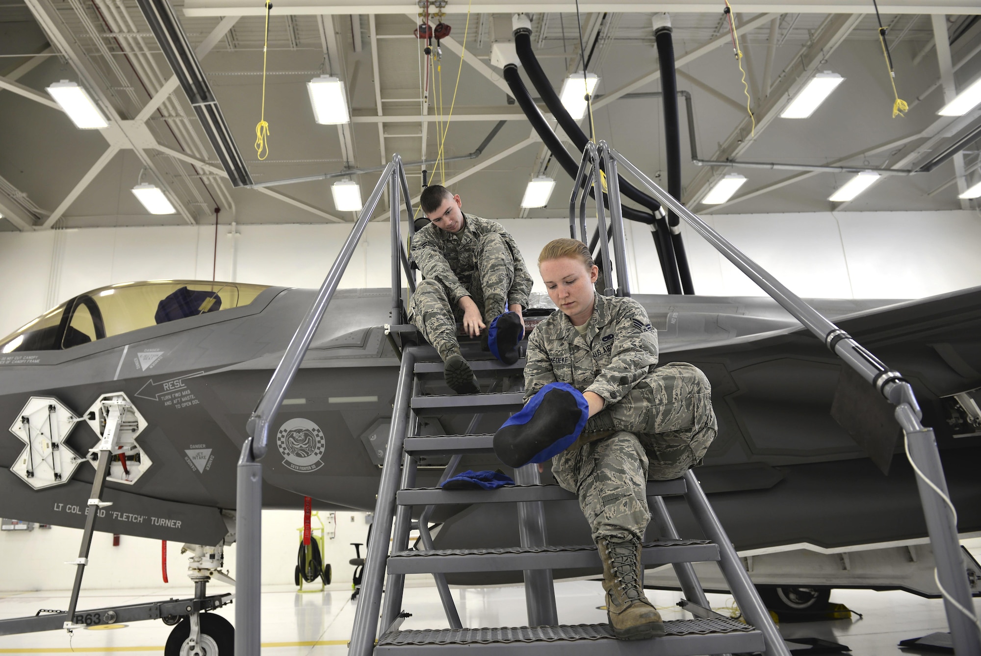 (Right) Senior Airman Samantha Schmedeke, 33rd Maintenance Squadron fuel systems journeyman, and (Left) Airman 1st Class William Manion, 33rd MXS fuel systems apprentice, put on booties before walking atop an F-35A Lightning II to perform maintenance at Eglin Air Force Base, Fla., May 16, 2016. Fuel systems specialists wear these protective coverings to avoid scuffing the low observable paint, which is part of the stealth effect on the jet. (U.S. Air Force photo/Senior Airman Andrea Posey)