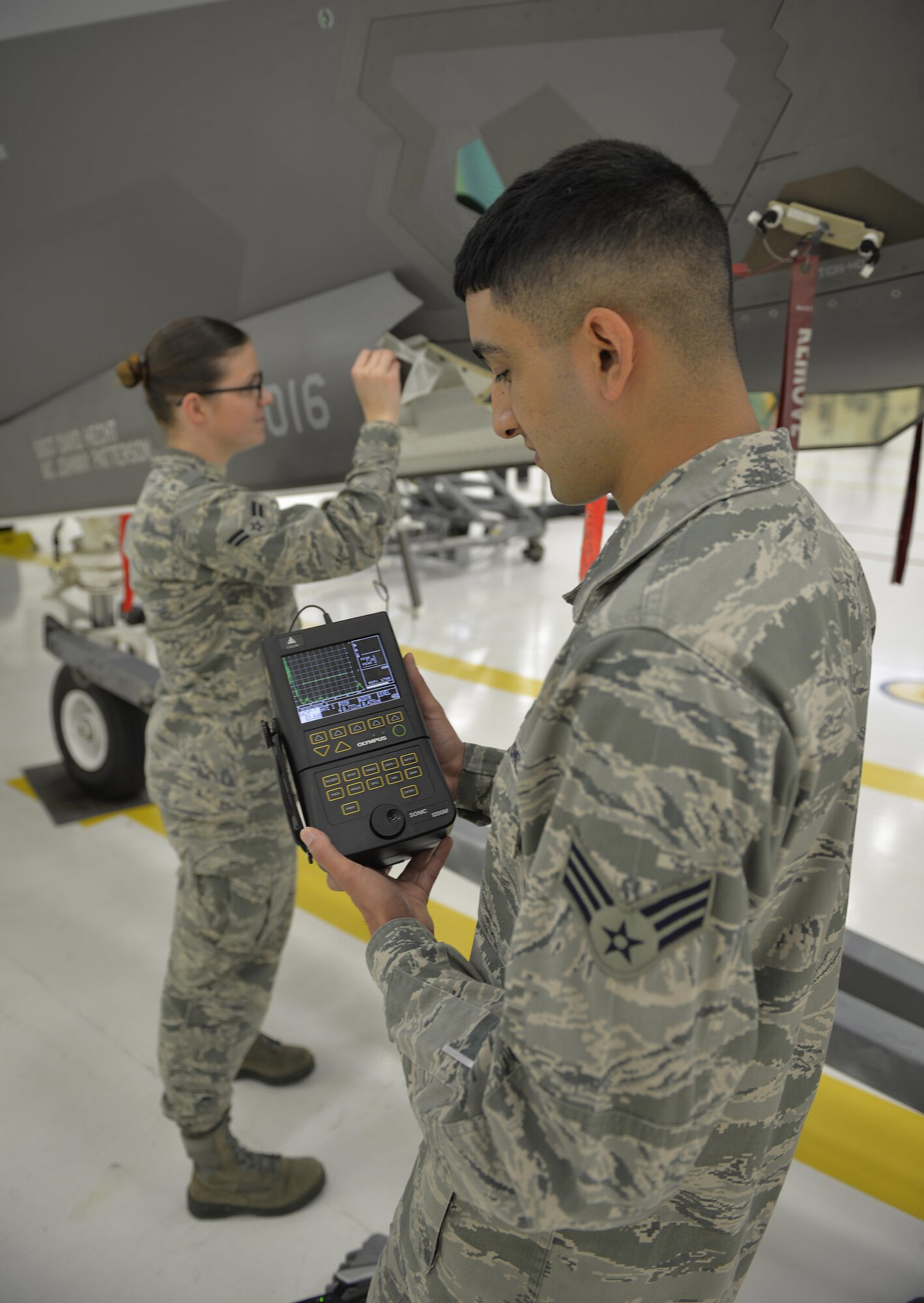 Senior Airman Santiago De La Rosa, 33rd Maintenance Squadron nondestructive inspection journeyman, assists Airman 1st Class Emily Greaves, 33rd MXS NDI apprentice, by monitoring the readings on a transducer, which looks for cracks in the low observable paint of an F-35A Lightning II at Eglin Air Force Base Fla., May 17, 2016. This practice ensures the effectiveness of the jet’s stealth capability by identifying any potential cracks.  (U.S. Air Force photo/Senior Airman Andrea Posey)