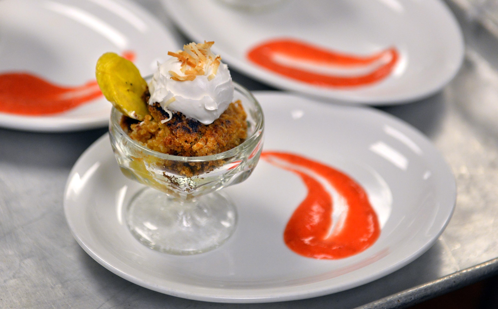 The culinary team representing the Ronald L. King Dining Facility created a pineapple crisp for their dessert dish during the Iron Chef Competition held at the King Dining Facility on June 2, Offutt Air Force Base, Neb.  The crisp was topped off with roasted coconut flakes, a handmade whipped cream, garnished with a plantain chip and plated with a decorative swoosh of strawberry puree.   (U.S. Air Force photo by Josh Plueger/Released)