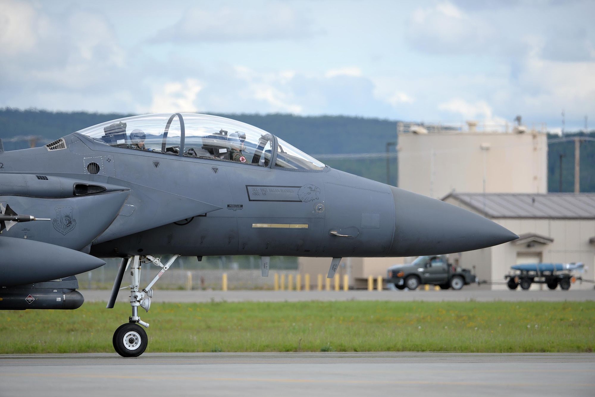 A U.S. Air Force F-15E Strike Eagle all-weather, highly maneuverable, dual-role fighter assigned to the 494th Fighter Squadron out of Royal Air Force Lakenheath, England, taxis down the Eielson Air Force Base, Alaska, flight line as an Airman transports a dummy munition in the background, June 6, 2016, during RED FLAG-Alaska (RF-A) 16-2. RF-A enables joint and international units like the Liberty Wing to sharpen their combat skills by flying simulated combat sorties in a realistic threat environment, which allows them to exchange tactics, techniques and procedures while improving interoperability. (U.S. Air Force photo by Master Sgt. Karen J. Tomasik/Released)