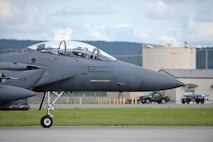 A U.S. Air Force F-15E Strike Eagle all-weather, highly maneuverable, dual-role fighter assigned to the 494th Fighter Squadron out of Royal Air Force Lakenheath, England, taxis down the Eielson Air Force Base, Alaska, flight line as an Airman transports a dummy munition in the background, June 6, 2016, during RED FLAG-Alaska (RF-A) 16-2. RF-A enables joint and international units like the Liberty Wing to sharpen their combat skills by flying simulated combat sorties in a realistic threat environment, which allows them to exchange tactics, techniques and procedures while improving interoperability. (U.S. Air Force photo by Master Sgt. Karen J. Tomasik/Released)