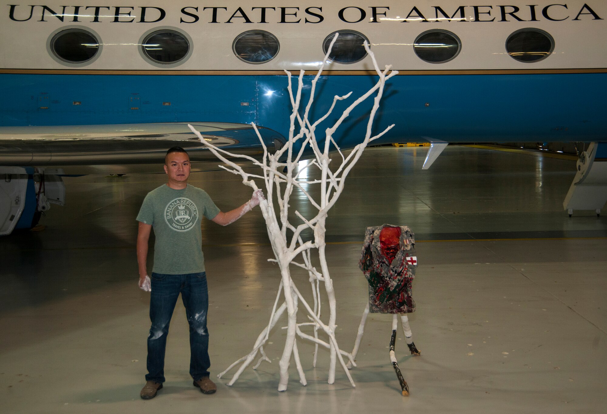 Retired Tech. Sgt. Steven Luu stands with his artwork in Hangar 4 at Joint Base Andrews, Md., May 25, 2016. The tall-standing tree piece (left), titled: The Day After Combat, and the Airman Battle Uniform top piece (right), titled: I Was a Medic, were created by Luu as part of an art therapy program while at Walter Reed National Medical Center, Md. (U.S. Air Force photo by Airman Gabrielle Spalding)