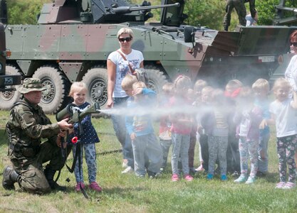 Pfc. Adrian Otwinowski, from the 5th Chemical Regiment, demonstrates to a local primary school student how to spray water from a decontamination tool in the town of Mielenko Drawskie, Poland during Exercise Anakonda  2016, a Polish-led, multinational exercise running from June 7-17. (U.S. Army photo by Spc. Miguel Alvarez/ Released)