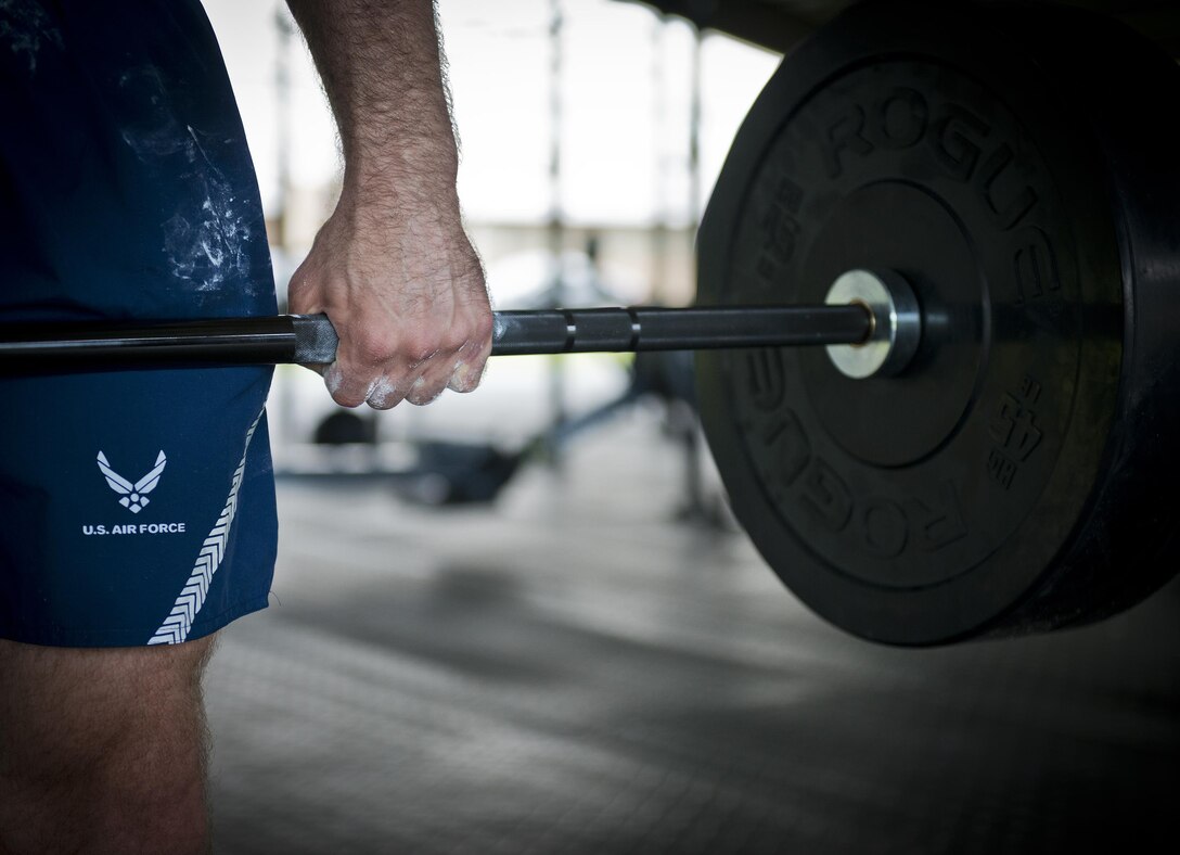 An athlete holds a weighted bar for as long as he can while his teammate performs calisthenics  during a team combat fit competition June 11 at Duke Field, Fla.  The three-round competition pushed the teams to their limits with repetitive weight lifting, rowing, sled-pulling and other kinetic activities.  (U.S. Air Force photo/Tech. Sgt. Sam King)