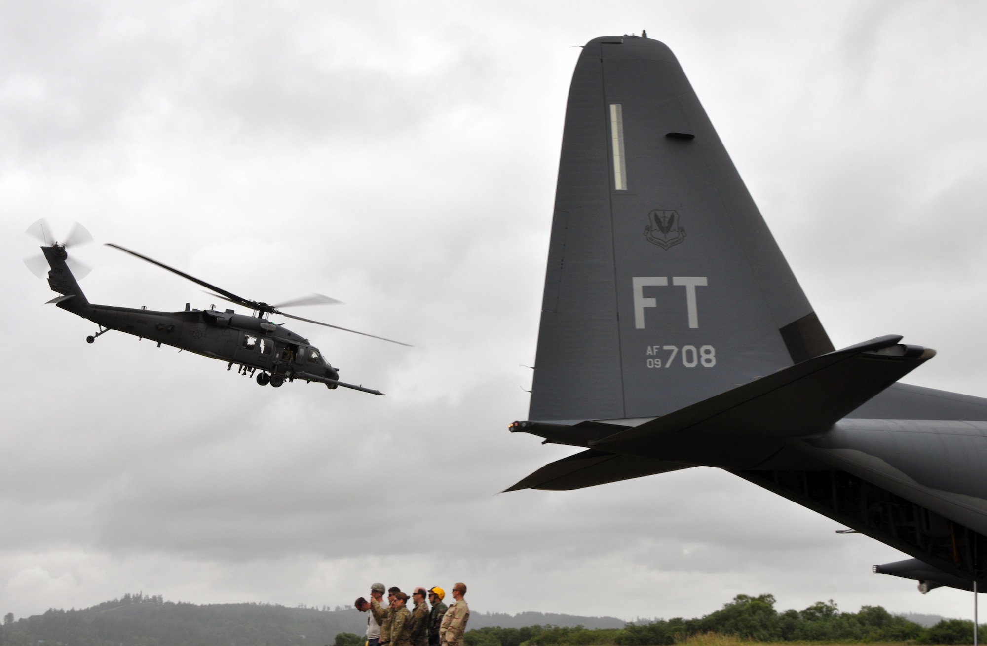 Reservists from the 304th Rescue Squadron, Portland Air National Guard Base, Ore., stand behind an HC-130 as they watch an HH-60G Pave Hawk helicopter from the 305th Rescue Squadron, Davis-Monthan Air Force Base, Ariz., depart the airport in Astoria, Ore., June 8, 2016. Several 304th personnel, plus Air and Army National Guardsmen and other local, state and federal government and civilian organizations participated in Cascadia Rising, a disaster response exercise simulating a magnitude 9.0 earthquake and subsequent tsunami in the Pacific Northwest. (U.S. Air Force photo by 1st Lt. Anna-Marie Wyant)
