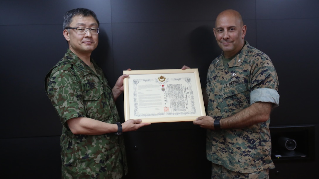U.S. Marine Col. Eric M. Mellinger, right, receives a certificate of appreciation and a Defense Cooperation Medal from Japanese Ground Self-Defense Force Col. Shusei Hotta on behalf of Gen. Kiyofumi Iwata, June 13, 2016, at Camp Courtney, Okinawa, Japan. Mellinger was awarded for significantly contributing to increased training opportunities for the JGSDF by advancing co-use of Marine Corps training facilities on Okinawa and expanding III Marine Expeditionary Force efforts to participate in alliance/bilateral exercises. Hotta is the deputy chief of Policy and Programs Division, Ground Staff Office, JGSDF. Iwata is JGSDF chief of staff. Mellinger is III MEF chief of staff.