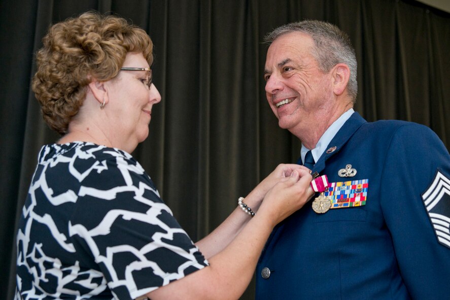 Rita Taylor, wife of retired Chief Master Sgt. Tim Taylor, attaches a lapel pin during his retirement ceremony at Little Rock Air Force Base, Ark., June 11, 2016. Chief Taylor retired after 36 years of faithful service to his country in a room filled with family, friends and co-workers. (U.S. Air Force photo by Master Sgt. Jeff Walston/Released)     