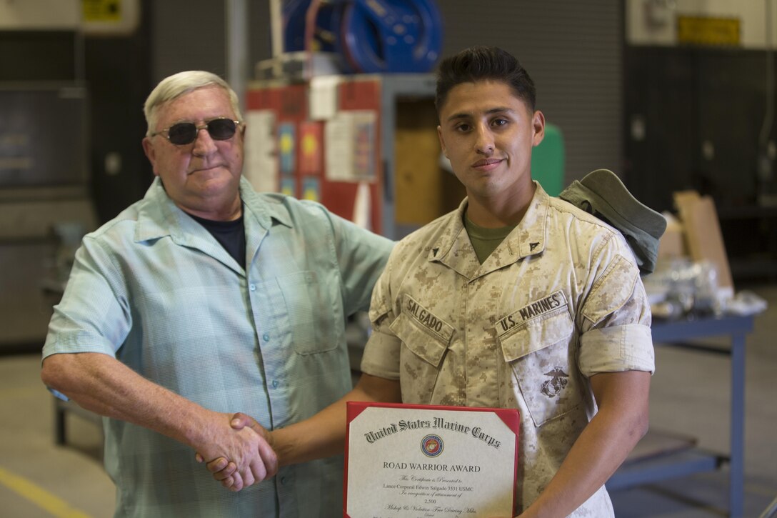 Lance Cpl. Edwin Salgado, motor transport operator, 7th Marine Regiment, is congratulated by Dan Mucuihill, tactical safety specialist, Safety Division, after receiving the Road Warrior Award in building 1951 June 2, 2016. The award is presented to any military or government civilian employee who operates government motor vehicles and achieves mishap or violation-free driving in 2,500-mile increments. (Official Marine Corps photo by Cpl. Medina Ayala-Lo/ Released)