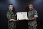 CAMP COURTNEY, Okinawa, Japan - U.S. Marine Col. Eric M. Mellinger, right, receives a certificate of appreciation and a Defense Cooperation Medal from Japanese Ground Self-Defense Force Col. Shusei Hotta on behalf of Gen. Kiyofumi Iwata, June 13, 2016, at Camp Courtney, Okinawa, Japan. Mellinger was awarded for significantly contributing to increased training opportunities for the JGSDF by advancing co-use of Marine Corps training facilities on Okinawa and expanding III Marine Expeditionary Force efforts to participate in alliance/bilateral exercises. Hotta is the deputy chief of Policy and Programs Division, Ground Staff Office, JGSDF. Iwata is JGSDF chief of staff. Mellinger is III MEF chief of staff.