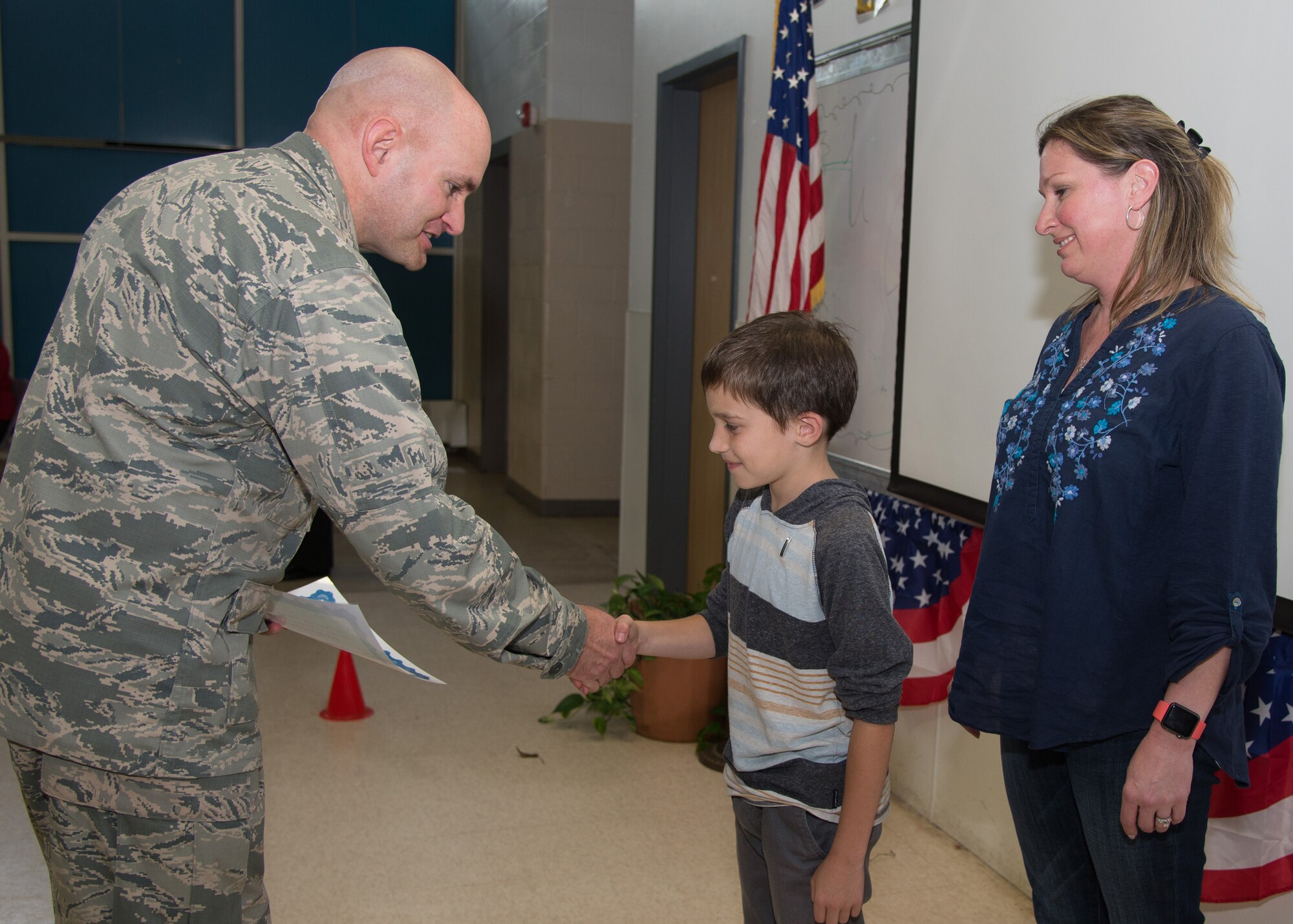 Col. David R. Dunklee, 66th Air Base Group commander, presents a certificate to Ethan Fisher, a Hanscom Primary School second grader, during a Reading Forces pinning ceremony at the school June 10, while his mom, Tina Carter, looks on. The Reading Forces program is a yearlong project that encourages nightly reading. Children enlist in the reading program and are required to read 500 minutes outside of school, they advance in rank the more they read. (U.S. Air Force photo by Mark Herlihy)