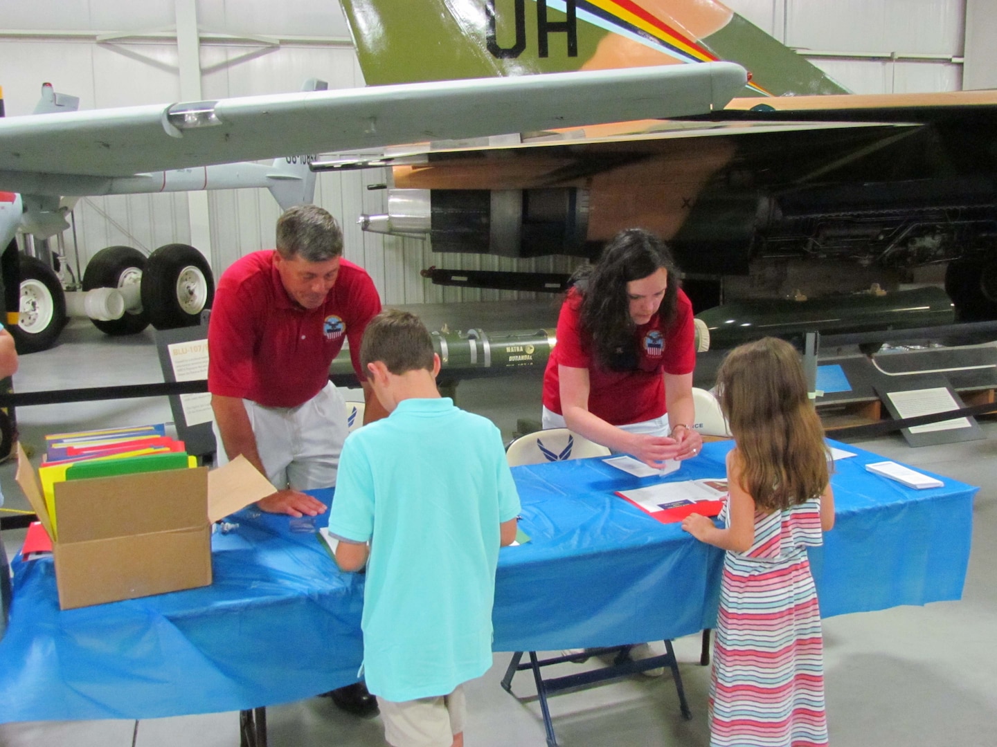 Defense Logistics Agency Aviation at Ogden, Utah, employees Scott Wilson and Kelly Scott greet children and provide them with welcome packets during the organization’s “Bring Your Child to Work Day” June 9, 2016, at the Hill Aerospace Museum on Hill Air Force Base. 