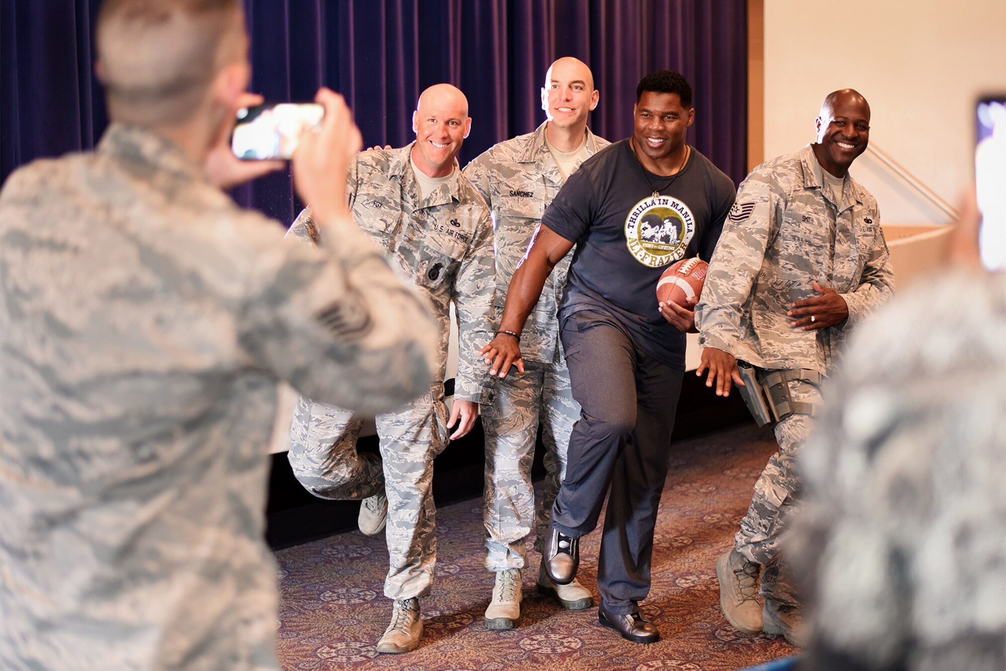 PETERSON AIR FORCE BASE, Colo. – Herschel Walker, retired NFL football player, strikes the Heisman pose with Team Pete service members in the base auditorium at Peterson Air Force Base, Colo. on June 8, 2016. Walker played college football for the University of Georgia, earned consensus All-American honors three times and won the 1982 Heisman Trophy. (U.S. Air Force photo by Airman 1st Class Dennis Hoffman)