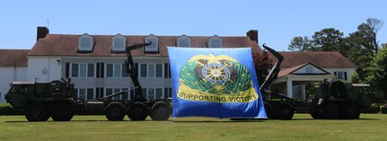 The Quartermaster Regimental Crest, supported between two Palletized Load System (PLS) vehicles, in front of the Lee Club, Fort Lee, Va., June 10, 2016. The regimental crest was placed in support of the United States Army Quartermaster School Regimental Honors Ceremony, an annual event that honors distinguished members and units of the Quartermaster Corps for their achievements at Fort Lee, Va., 10 June, 2016.