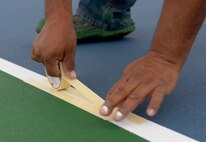 Rafael Mendez, Renner Sports Surfaces painter, applies tape to the multipurpose sport courts lines at Ellsworth Air Force Base, S.D., June 14, 2016. The 28th Force Support and 28th Civil Engineer Squadrons teamed up to resurface the courts, providing an outdoor location for activities such as tennis, basketball and volleyball. (U.S. Air Force photo by Airman Donald Knechtel/Released)