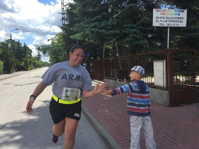 U.S. Army Reserve Sgt. Jennifer Hoeppner, a human resource specialist with the 364th Expeditionary Sustainment Command Marysville, Washington high fives a young Polish resident during a 10-kilometer race in Sulejowek, Poland.  The 364th is participating in Anakonda 16, a Polish-led national event that seeks to train, exercise and integrate Polish national command and force structures into an Allied, joint, multinational environment. (Photo by Capt. A. Sean Taylor, 649th RSG)