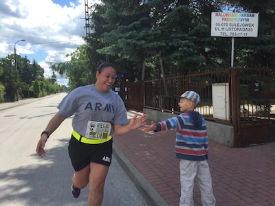 U.S. Army Reserve Sgt. Jennifer Hoeppner, a human resource specialist with the 364th Expeditionary Sustainment Command Marysville, Washington high fives a young Polish resident during a 10-kilometer race in Sulejowek, Poland.  The 364th is participating in Anakonda 16, a Polish-led national event that seeks to train, exercise and integrate Polish national command and force structures into an Allied, joint, multinational environment. (Photo by Capt. A. Sean Taylor, 649th RSG)