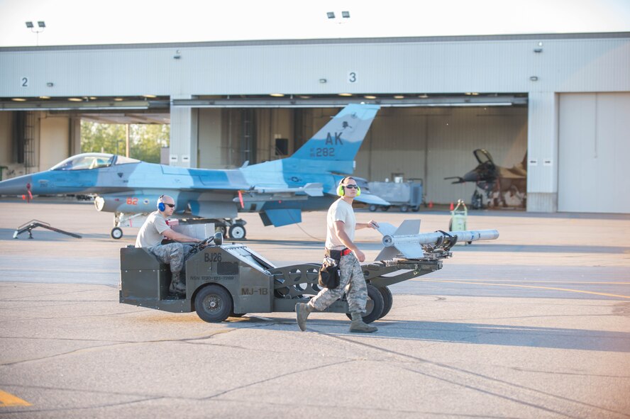 U.S. Air Force Staff Sgt. Nathan Mendoza escorts Airman 1st Class Tyler Lounds, both aircraft armament systems technicians from the 354th Maintenance Squadron, as Tyler drives the MJU-1 Jammer munition vehicle on the way to an F-16 Fighting Falcon fighter aircraft while working swing shift June 14, 2016, during RED FLAG-Alaska (RF-A) 16-2 at Eielson Air Force Base, Alaska. Jets are flown almost double the normal hours during RF-A, increasing the need for maintenance, which provides training for support personnel in sustainment of large-force deployed air operations. (U.S. Air Force photo by Staff Sgt. Shawn Nickel/Released)

