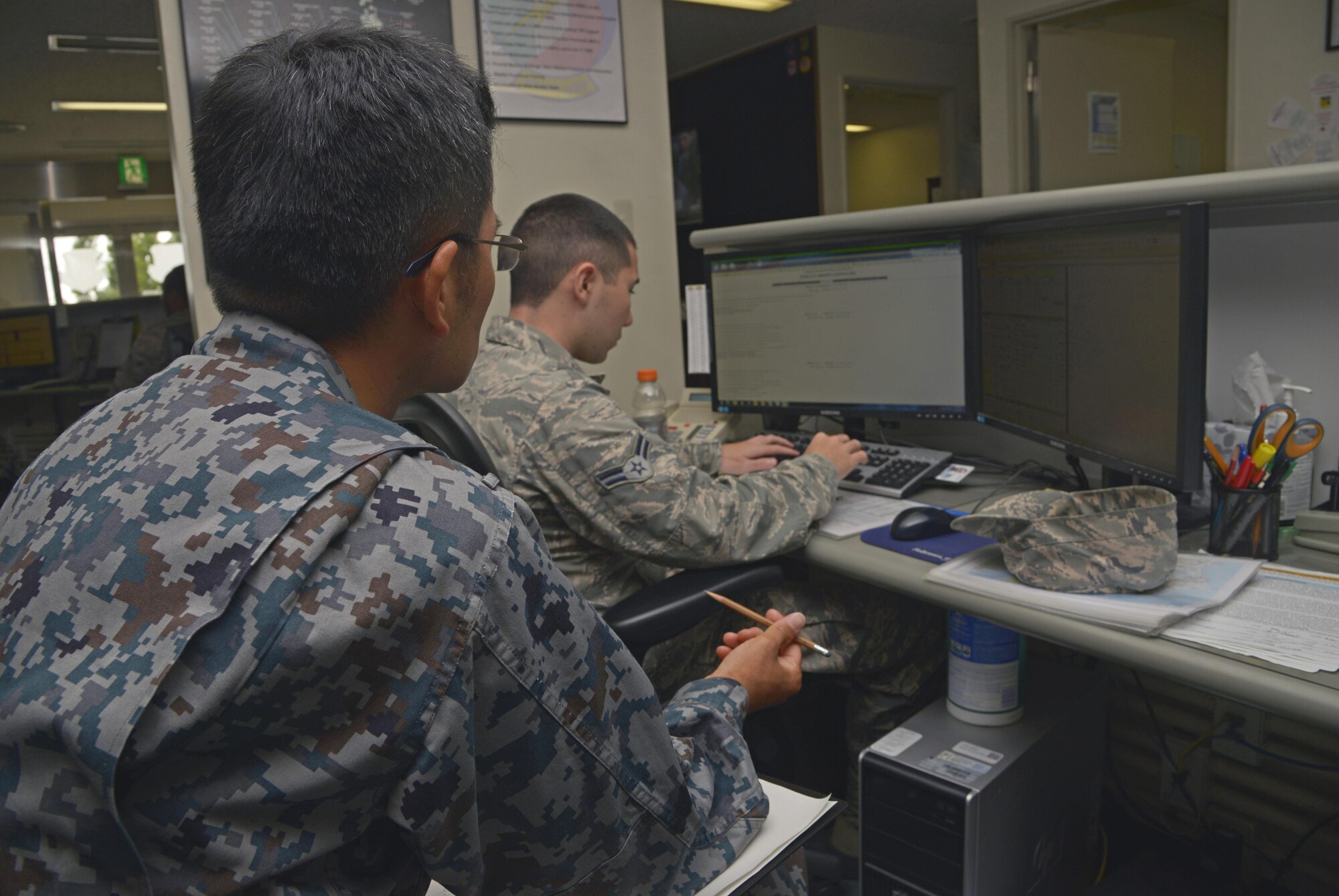 Capt. Naoki Nishino, Japan Air Self-Defense Force weather station forecaster, watches Airman 1st Class Ryan Gooch, 374th Operations Support Squadron weather flight weather apprentice, as he reviews weather briefing notes at Yokota Air Base, Japan, June 14, 2016. The weather brief informs pilots of what to expect on upcoming flight missions. (U.S. Air Force photo by Senior Airman David Owsianka/Released)