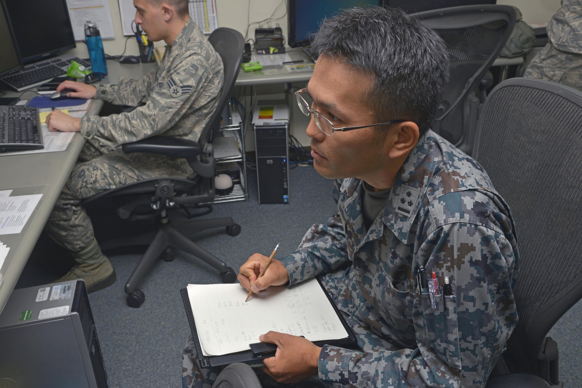 Capt. Naoki Nishino, Japan Air Self-Defense Force weather station forecaster, takes notes as Airman 1st Class Ryan Gooch, 374th Operations Support Squadron weather flight weather apprentice, as he reviews weather briefing notes at Yokota Air Base, Japan, June 14, 2016. The weather brief informs pilots of what they'll expect on upcoming flight missions. (U.S. Air Force photo by Senior Airman David Owsianka/Released)