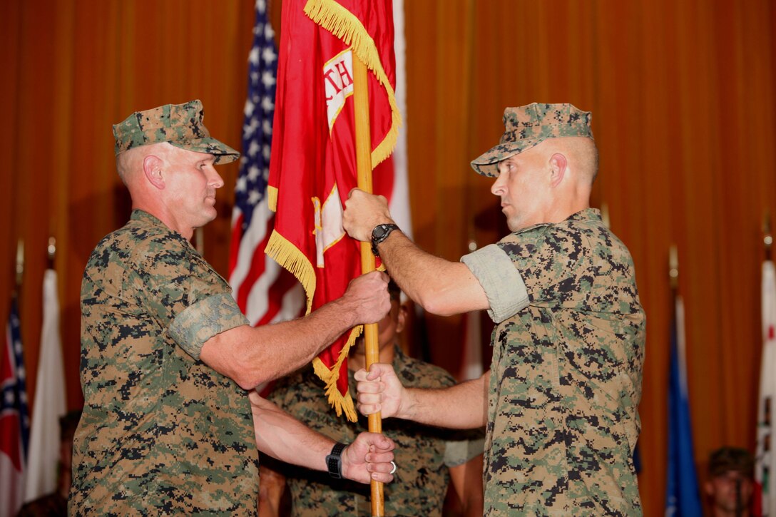 Col. David L. Odom, right, passes the 4th Marine Regiment colors to Col. Kevin A. Norton, left, June 16 at the theater on Camp Schwab.