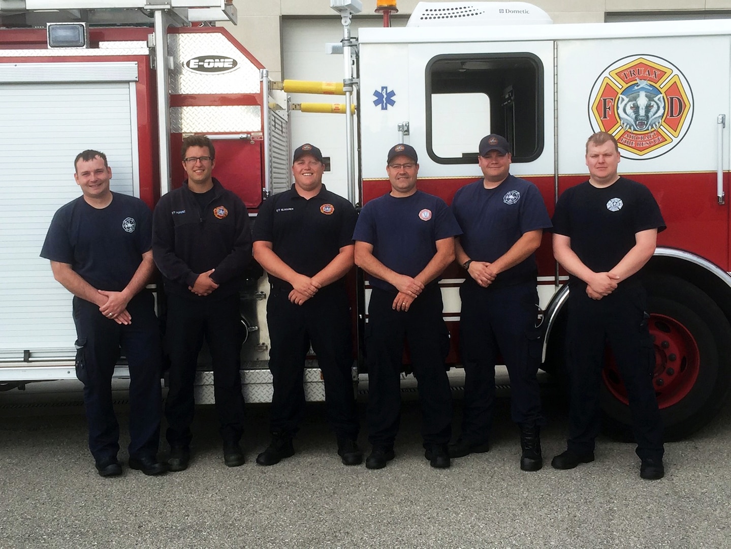 A team of firefighters from the 115th Fighter Wing Truax Fire and Emergency Services pose for a photo outside thier fire truck in Madison, Wis., June 6, 2016. This team of firefighters helped save a woman's life by performing cardiopulmonary resuscitation after she collapsed on a jet.