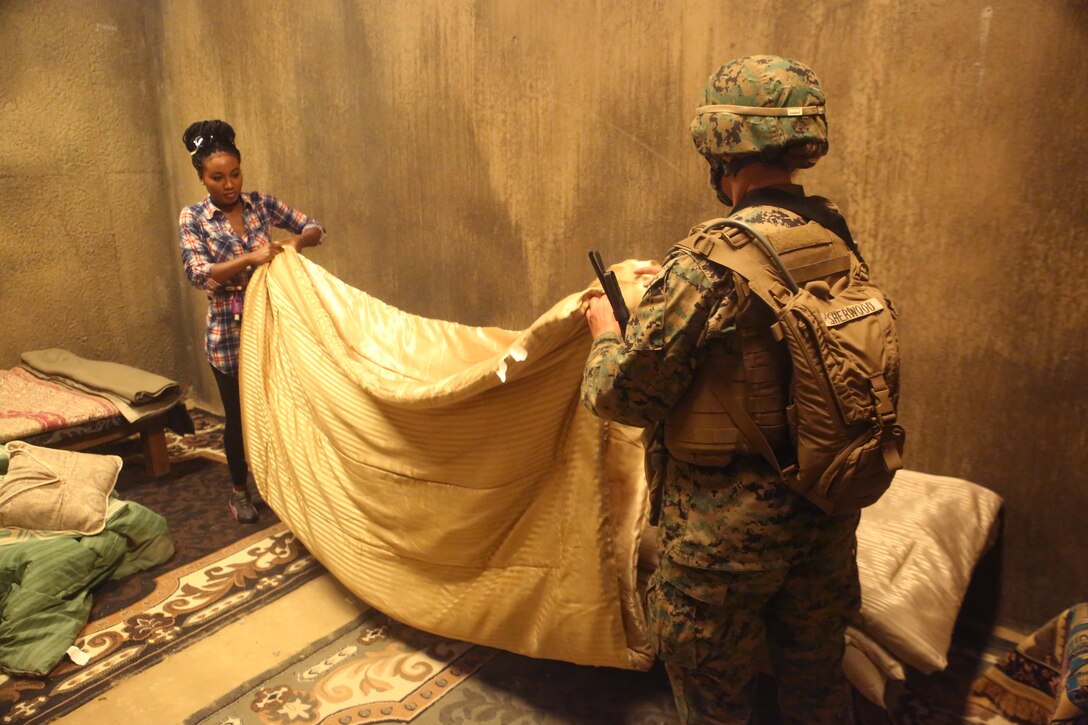 A Marine with 2nd Civil Affairs Group helps a role player fold a blanket in a notional West African village during a training exercise that integrated 2nd CAG and II Marine Expeditionary Force Camp Lejeune, N.C., June 12, 2016. The training was designed to have the civil affairs specialists assess the damages and needs of villagers in a war-torn environment. (U.S. Marine Corps photo by Cpl. Joey Mendez/Released)