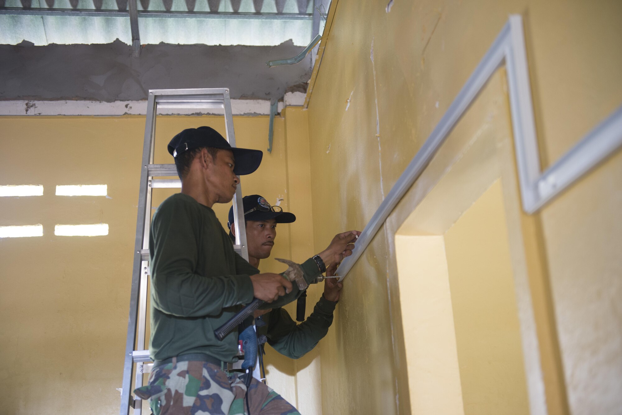 Cambodian Armed Forces Sgt. Nget Sytha and Sgt. Ngin Samnang, Royal Cambodian engineers fit the wall of a health center for electrical cables during Pacific Angel 16-2, June 16, 2016, in Kampot Province, Cambodia. Pacific Angel is a humanitarian assistance/civil military operation missions that builds partner capacity through medical/health outreach, engineering civic projects and subject matter exchanges. (U.S. Air Force photo by Senior Airman Omari Bernard/Released)