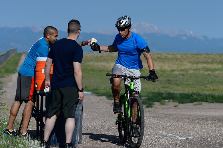 Jacob Lacefield grabs a cup of water from a volunteer while biking during the 12th annual duathlon at Schriever Air Force Base, Colorado, Friday, June 17, 2016. Volunteers for the event were stationed at regular intervals to assist participants in navigating the course. (U.S. Air Force photo/Christopher DeWitt)
