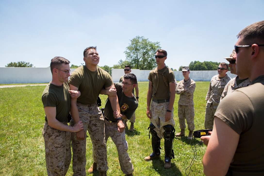 Lance Cpl. Johnny T. Banuelos (second from left), a military policeman with 4th Law Enforcement Battalion, Force Headquarters Group, Marine Forces Reserve, is guided to ground after being tased during non-lethal weapons training at the Muscatatuck Urban Training Center in Butlerville, Ind., June 11, 2016. It is important for Marines to understand how to effectively operate gear they carry and how it will affect the body once administered.  (U.S. Marine Corps photo by Lance Cpl. Melissa Martens/ Released) 