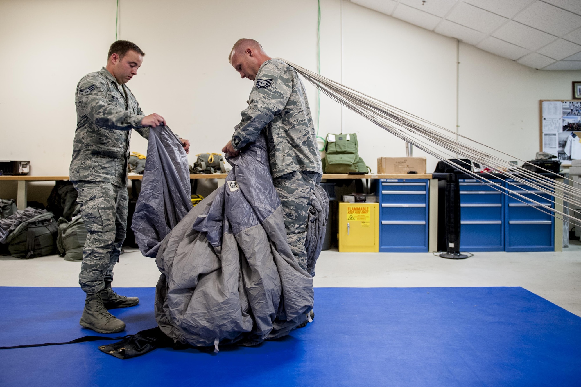 U.S. Air Force Senior Airman Erik Merrill, 31st Rescue Squadron aircrew flight equipment journeyman, and Tech. Sgt. Matthew Michels, 31st RQS aircrew flight equipment assistant NCO in charge, fold a parachute canopy June 20, 2016, at Kadena Air Base, Japan. Merrill and Michels ensure the safety of aircrews jumping from aircraft by assembling and maintaining parachute packs according to strict guidelines and procedures. (U.S. Air Force photo by Senior Airman Peter Reft)