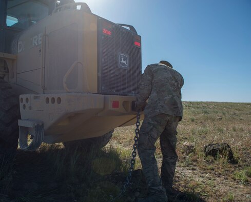 An airman from the 366th Civil Engineer Squadron attaches a chain to a shovel loader in preparation for removal of inert GBU-12 Paveway II during a range clearance at Saylor Creek Range Complex, Idaho, May 9, 2016. The GBU-12s were dropped during training exercises to improve fighter pilots' accuracy. (U.S. Air Force photo by Airman 1st Class Chester Mientkiewicz/Released)