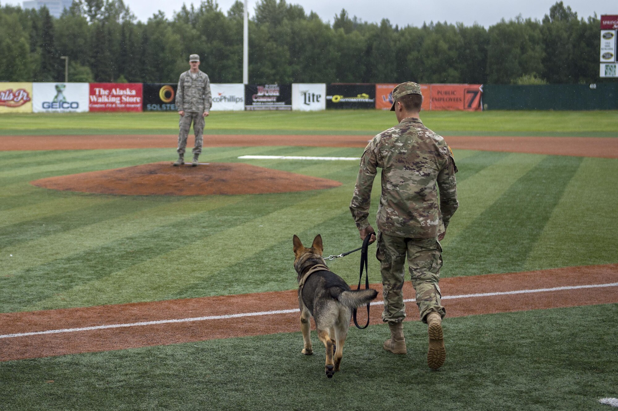 U.S. Army Private 1st Class Ian Smith and Military Working deliver the game ball to Airman 1st Class Logan Stuckey for the ceremonial first pitch during the Anchorage Bucs Military Appreciation Game at Mulcahy Stadium in Anchorage, Alaska, June 19, 2016. (U.S. Air Force photo by Senior Airman James Richardson/Released)
