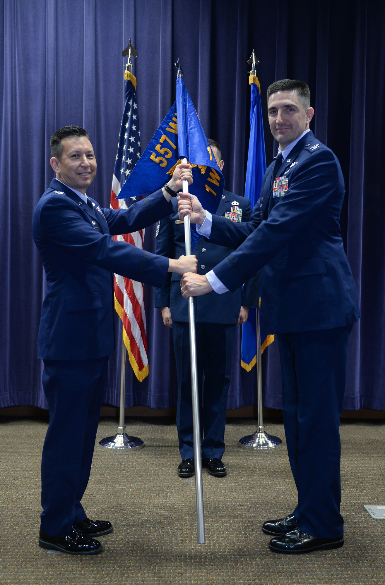 Col. William Carle, 557th Weather Wing commander, passes the guidon to Col. Thomas Blazek as he assumes command of the 1st Weather Group in the 557th Weather Wing auditorium June 21 at Offutt Air Force Base, Neb. (U.S. Air Force by Zachary Hada)