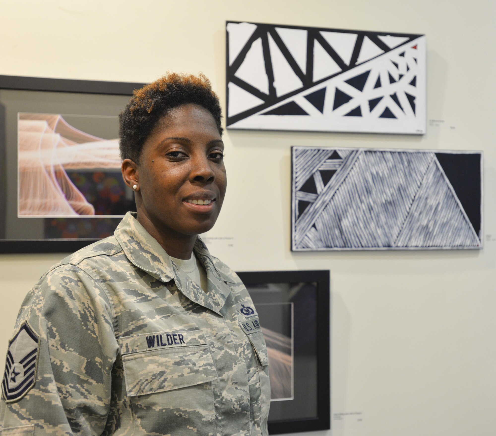 Master Sgt. Bahiya Wilder, 60th Operations Support Squadron aircrew flight equipment quality assurance flight chief, stands with two of her paintings June 22 at a gallery at the Solano Town Center Mall in Fairfield, Calif. 