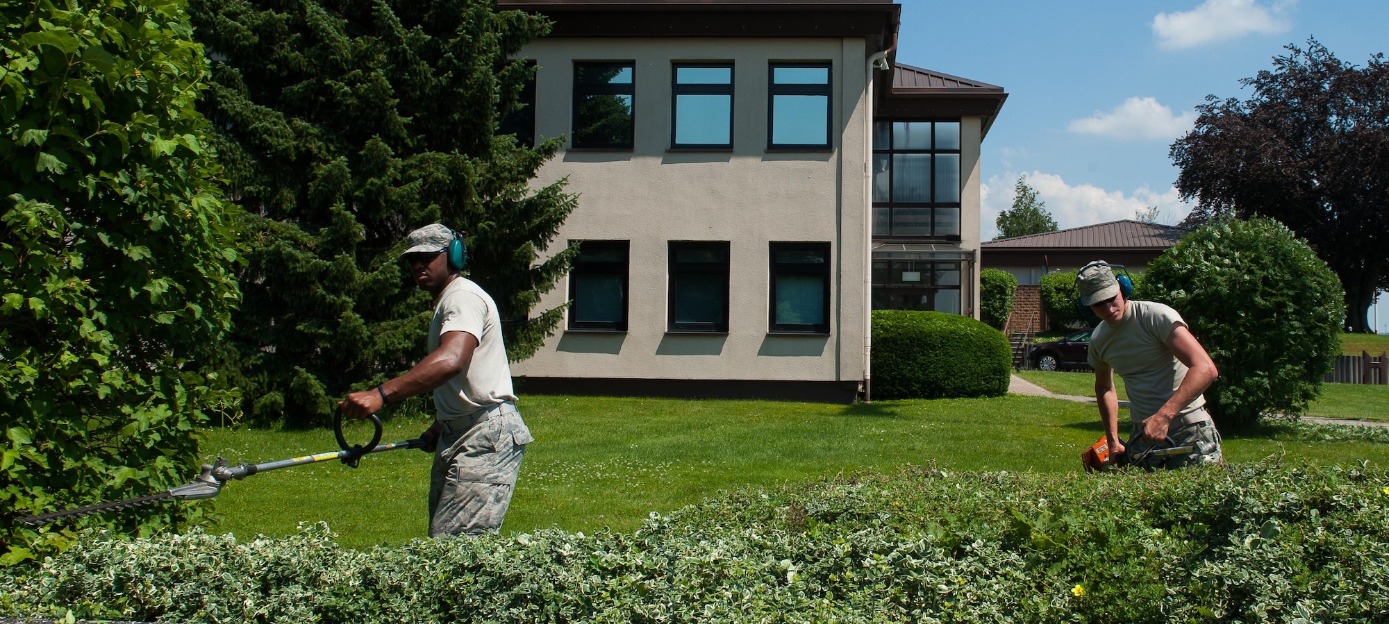Senior Airman Pascal Dieujuste and Airman 1st Class Daniel Collins, 786th Civil Engineering Squadron heavy equipment operatiors, pavement and construction specialist journeymen, trim bushes around Ramstein Air Base, Germany, June 24, 2016. Throughout the year, Ramstein maintains its high standard of cleanliness through the help of Airmen from the 786th CES and other squadrons maintaining base morale. (U.S. Air Force photo/Airman 1st Class Lane T. Plummer)