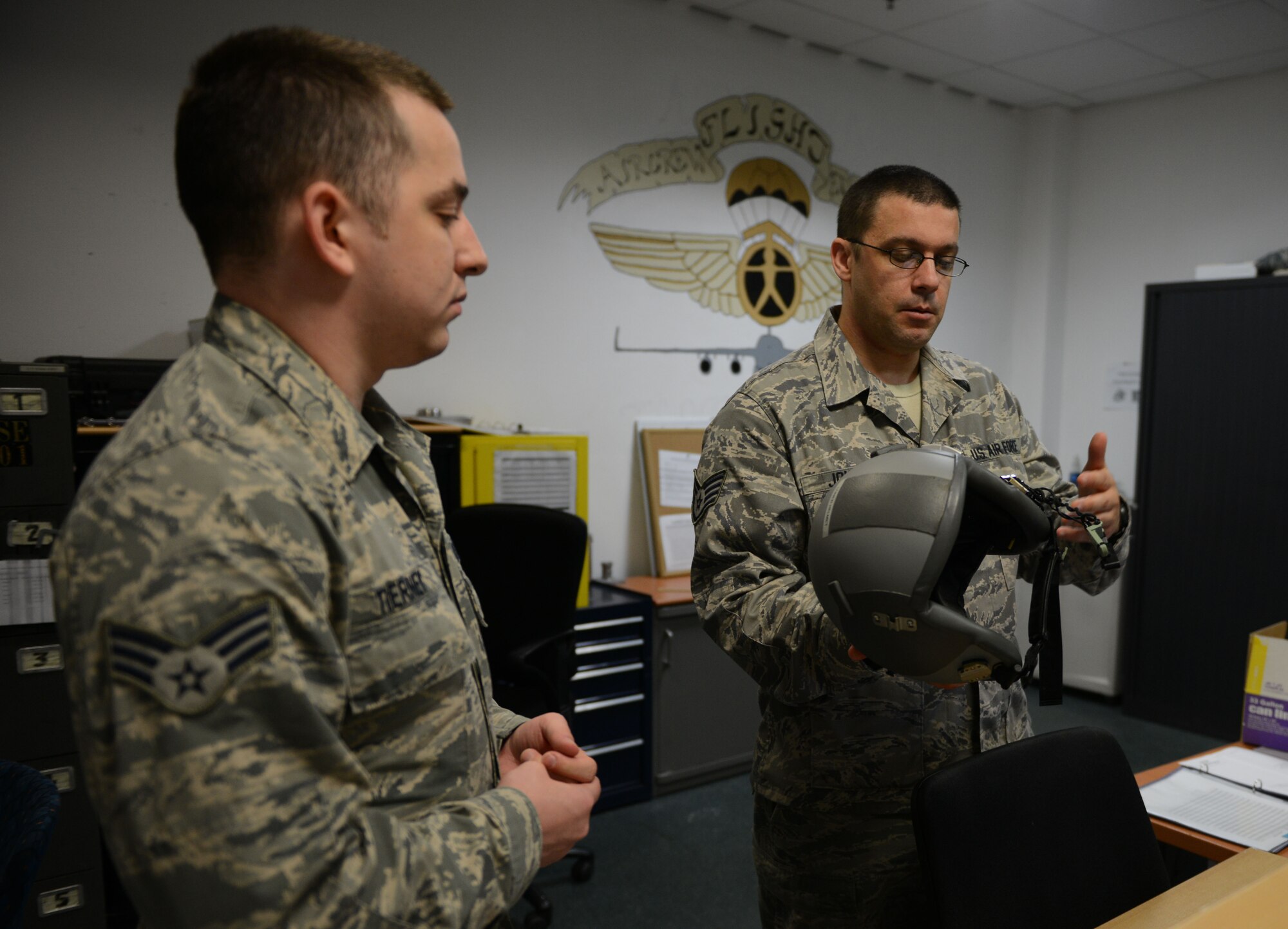 Staff Sgt. Jacob Johnson and Senior Airman Casey Tierney, 313th Expeditionary Operations Support Squadron aircrew flight equipment members, explain the features of a flight helmet at Ramstein Air Base, Germany, June 21, 2016. Both Johnson and Tierney are deployed to Ramstein as part of the 313th EOSS from Dover Air Force Base.  (U.S.  Air Force photo/ Airman 1st Class Joshua Magbanua)