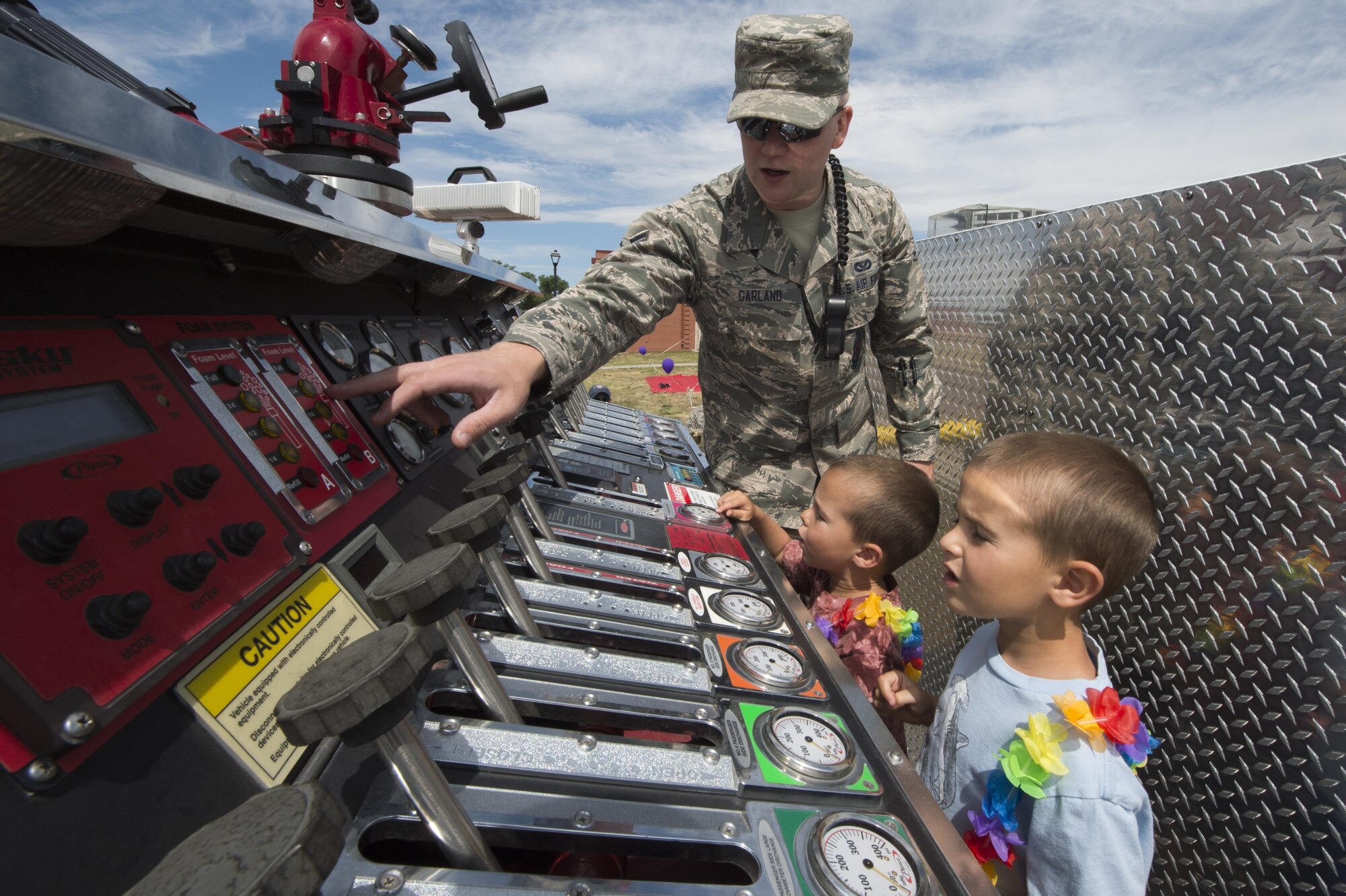 Airman 1st Class Dustin Garland, 90th Civil Engineering Squadron firefighter, explains the water pressure controls of a fire truck to Finnegan and Oliver Fournier, sons of Cody Fournier, East High School English teacher, during the Joint Services Multicultural Event at F.E. Warren Air Force Base, Wyo., June 22, 2016. An activity area with activities and bounce houses was available for children to enjoy. (U.S. Air Force photo by Staff Sgt. Christopher Ruano)