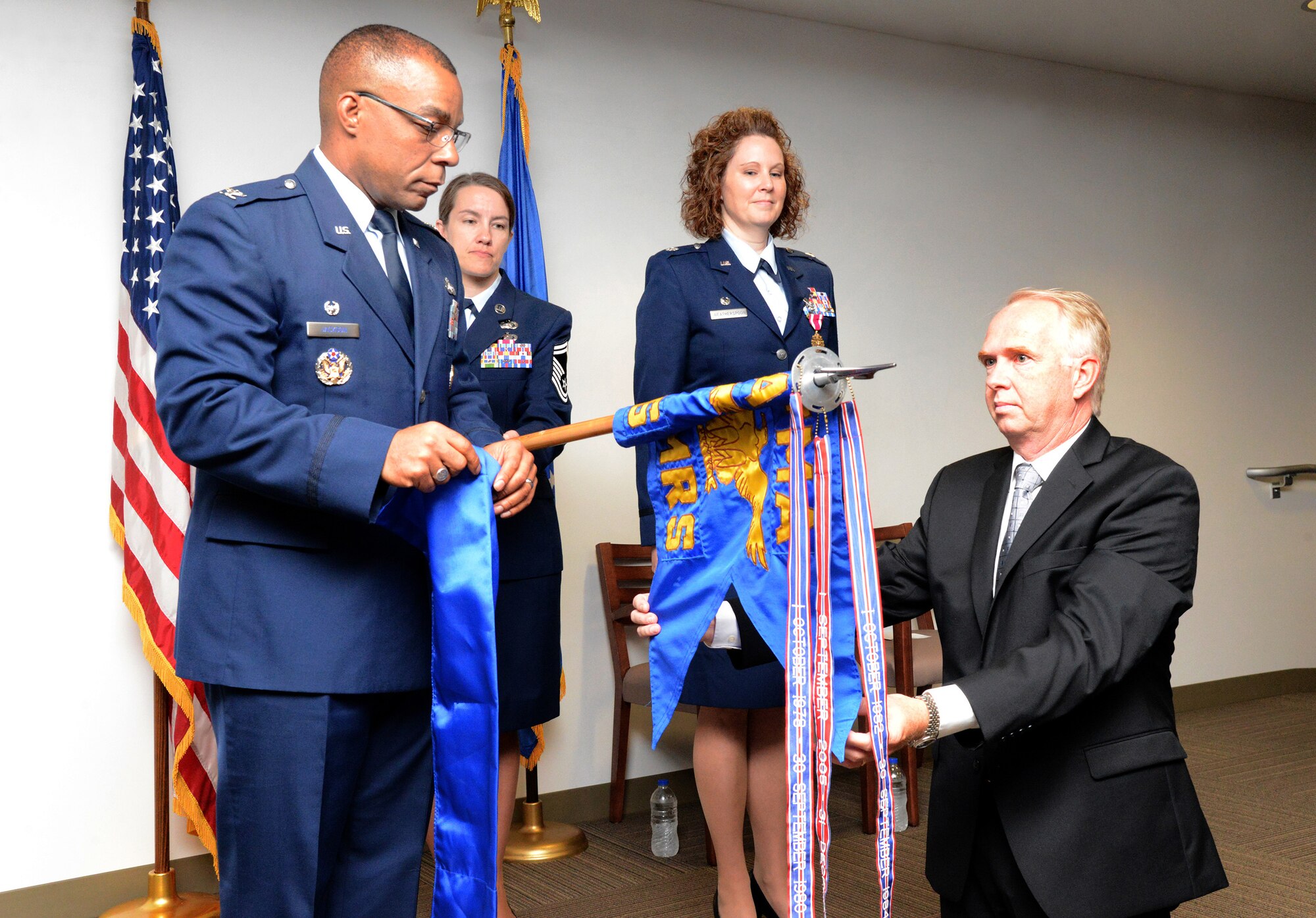 Col. Robert Jackson, Sr., commander of the Air Force Manpower Analysis Agency at Joint Base San Antonio-Randolph, Texas, left, along with Steve Davis, right, roll up and sleeve the guidon for the 5th Manpower Requirements Squadron during an inactivation ceremony on June 17. Mr. Davis was an original member of the 5th MRS, first known as the Air Force Maintenance and Supply Management Engineering Team, when it was activated on April 2, 1976. Senior Master Sgt. Stacey Isaac-Pickett, center left, was the guidon bearer of the ceremony in which Lt. Col. Dyann Weatherspoon was relieved of command of the 5th MRS. (Air Force photo by Kelly White/Released)