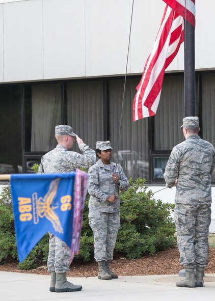 Senior Airman Nicholas Guarente salutes the flag as Staff Sgt. Natasha Steffen, left, and Staff Sgt. Dana Moffett, 66th Comptroller Squadron members, retrieve the flag during a retreat ceremony outside Building 1305 on base June 23. Retreat is played to mark the end of the duty day and precedes the playing of the national anthem. (U.S. Air Force photo by Walter Santos)