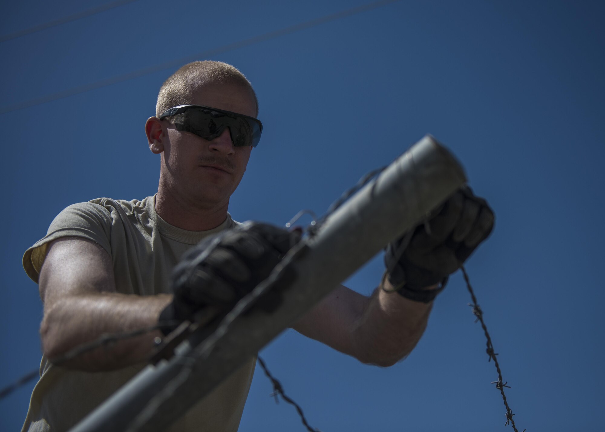 1st Lt. Mark Bohme, 455th Expeditionary Civil Engineer Squadron project engineer, unclips barb wire from a fence post during a building demolition, June 22, 2016, Bagram Airfield, Afghanistan. Developmental engineers plan, organize, and implement systems engineering processes as well as identify and incorporate new technology. (U.S. Air Force photo by Senior Airman Justyn M. Freeman)