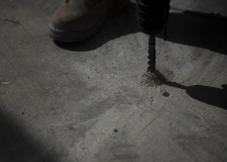 Airman 1st Class Taylor Davis, 455th Expeditionary Civil Engineer Squadron structural journeyman, drills holes in the ground, June 25, 2016, Bagram Airfield, Afghanistan. The holes in the ground allow the tent doors to stay shut once the stakes are lowered. (U.S. Air Force photo by Senior Airman Justyn M. Freeman)