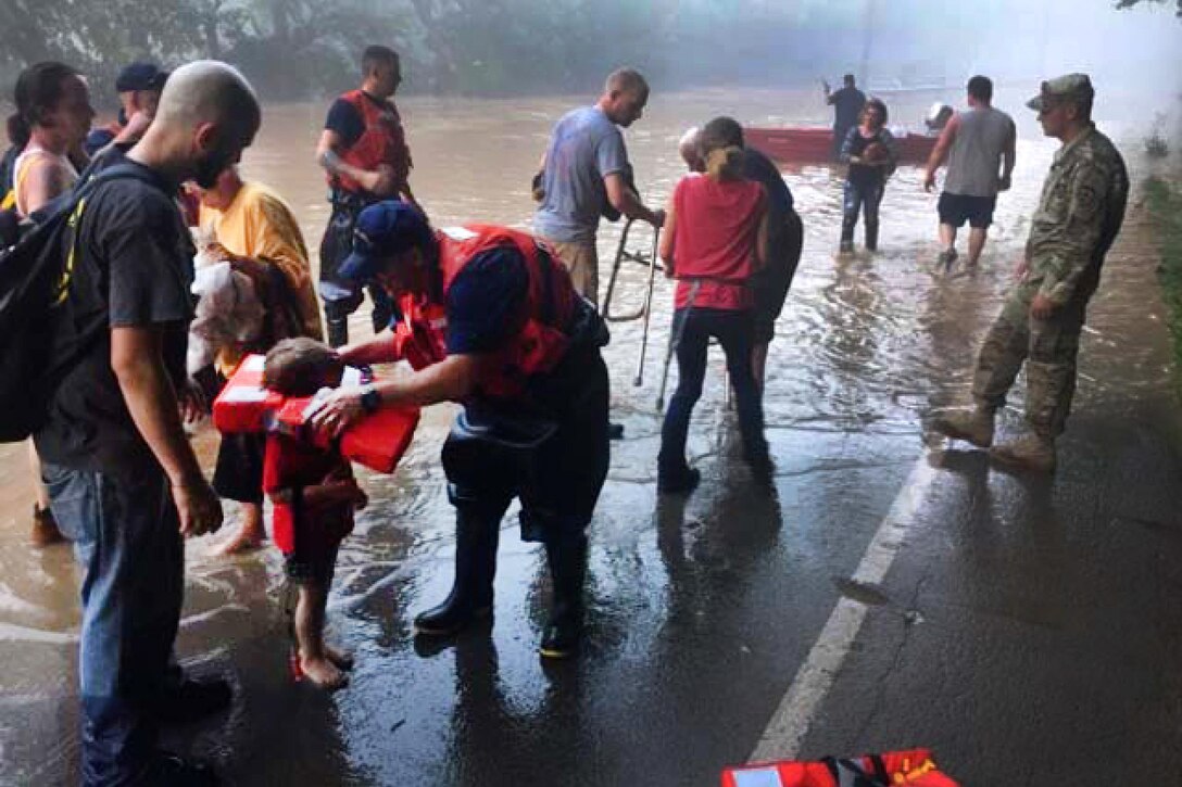 Coast Guardsmen and Army National Guardsmen provide life jackets to stranded residents before escorting them to a waiting vehicle during severe flooding in near Clendenin, W.V., June 24, 2016. The Coast Guardsmen, assigned to the Marine Safety Unit Huntington’s Western River Flood Punt Team, are assisting West Virginia state responders by providing disaster and relief assistance in response to widespread flooding. Coast Guard photo