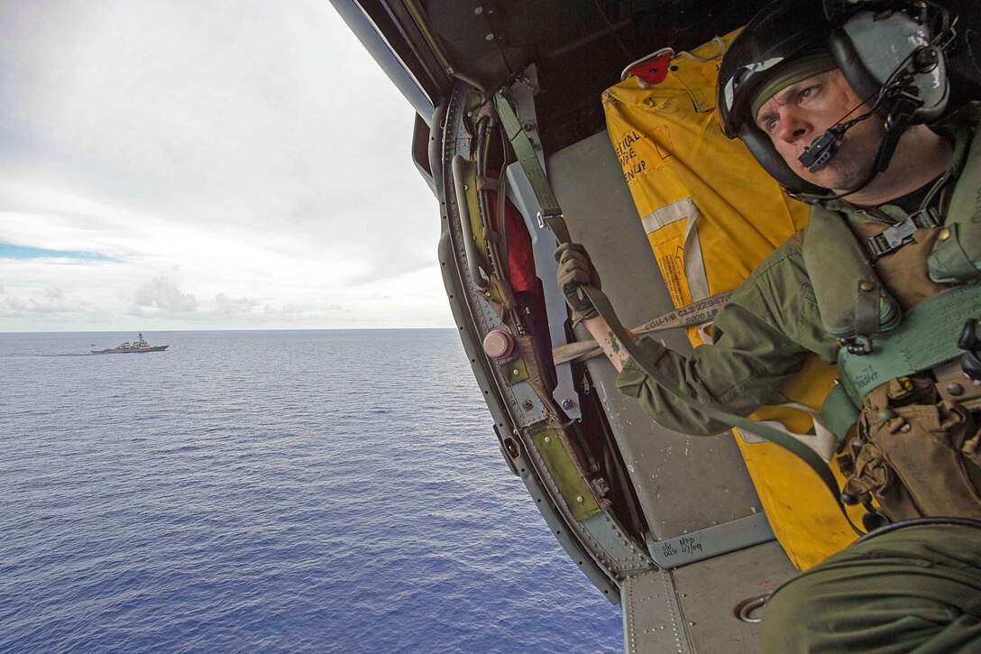 Navy Petty Officer 1st Class Justin Wright mans a rescue hoist aboard an MH-60S Sea Hawk helicopter and flies past the Arleigh Burke-class guided-missile destroyer USS Curtis Wilbur during combat search and rescue training in the Philippine Sea, June 26, 2016. Navy photo by Petty Officer 1st Class Elijah G. Leinaar