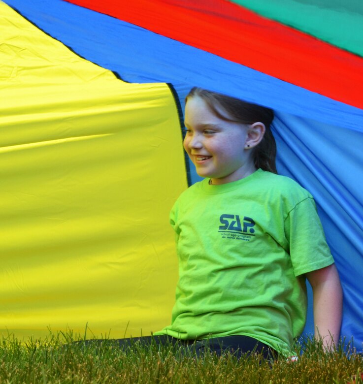 Sarah Ford sits under a parachute during a field day event at Schriever Air Force Base, Colorado, Monday, June 27, 2016. The parachute, which teaches students about the science behind how it works through an interactive experience, was one of many educational stations Schriever School Age Care and Ellicott summer program youth were able to participate in during the collaborative event. (U.S. Air Force photo/Brian Hagberg)