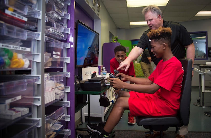 Ron McCermott, Raytheon engineer manager, teaches children how to use a flight simulator during the opening of the Center of Innovation at the Joint Base Andrews Youth Center, here, June 24, 2016. The center’s goal is to excite children about science, technology, engineering, and math subjects, also known as STEM. (U.S. Air Force photo by Senior Airman Mariah Haddenham)