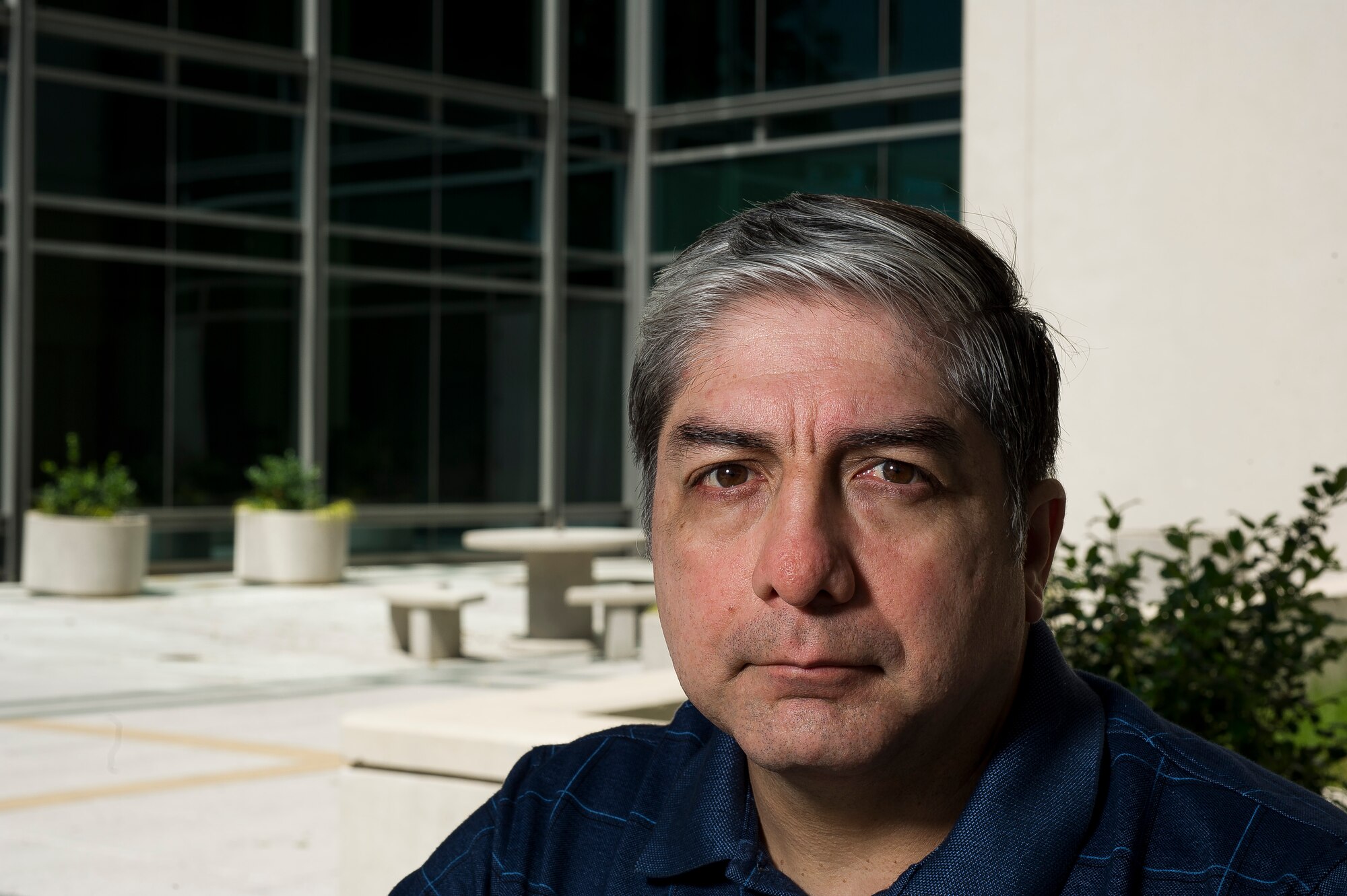 Alfredo Guerrero sits in front of the Defense Threat Reduction Agency building at Fort Belvoir, Va., on June 10, 2016, where he works as the anti-terrorism program manager. Guerrero was on top of Bldg. 131 of the Khobar Towers complex in Dharan, Saudi Arabia, on June 25, 1996, when he spotted a suspicious large gas truck drive toward the building. When the truck parked and two men jumped out and got into a car that had been following them, Guerrero and two other Airmen immediately began evacuating the building. A short time later the truck exploded, killing 19 Airmen and injuring more than 350 people. (U.S. Air Force photo/Staff Sgt. Christopher Gross)